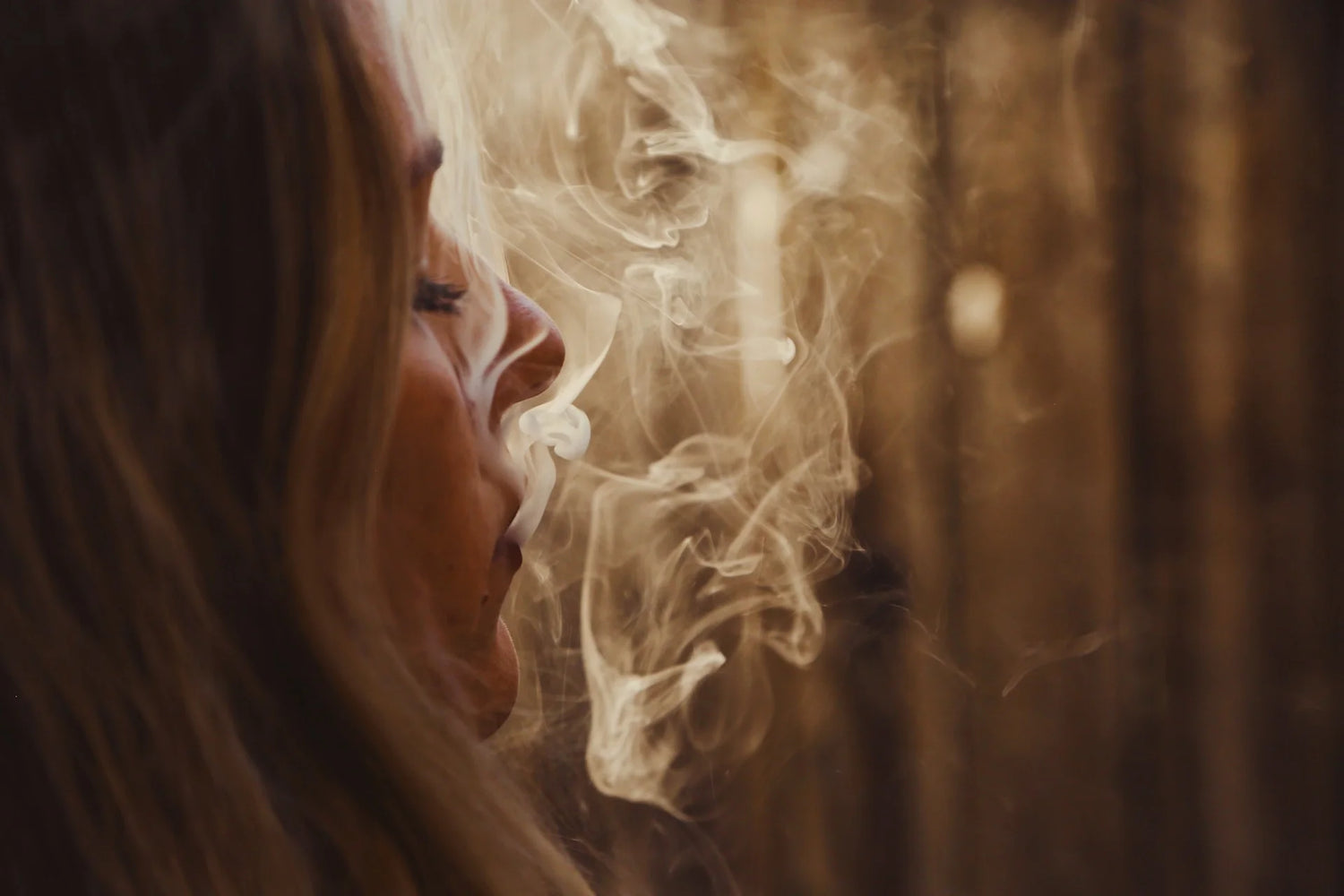 Blond girl exhaling white smoke from smoking a vape