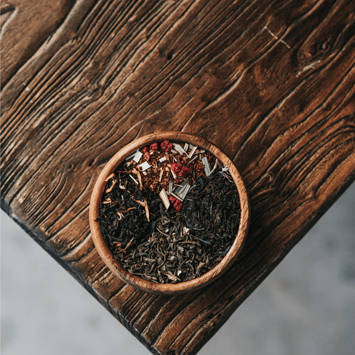 Close up of a mix of dried herbs displayed in a small wooden bowl on the corner of a wooden table